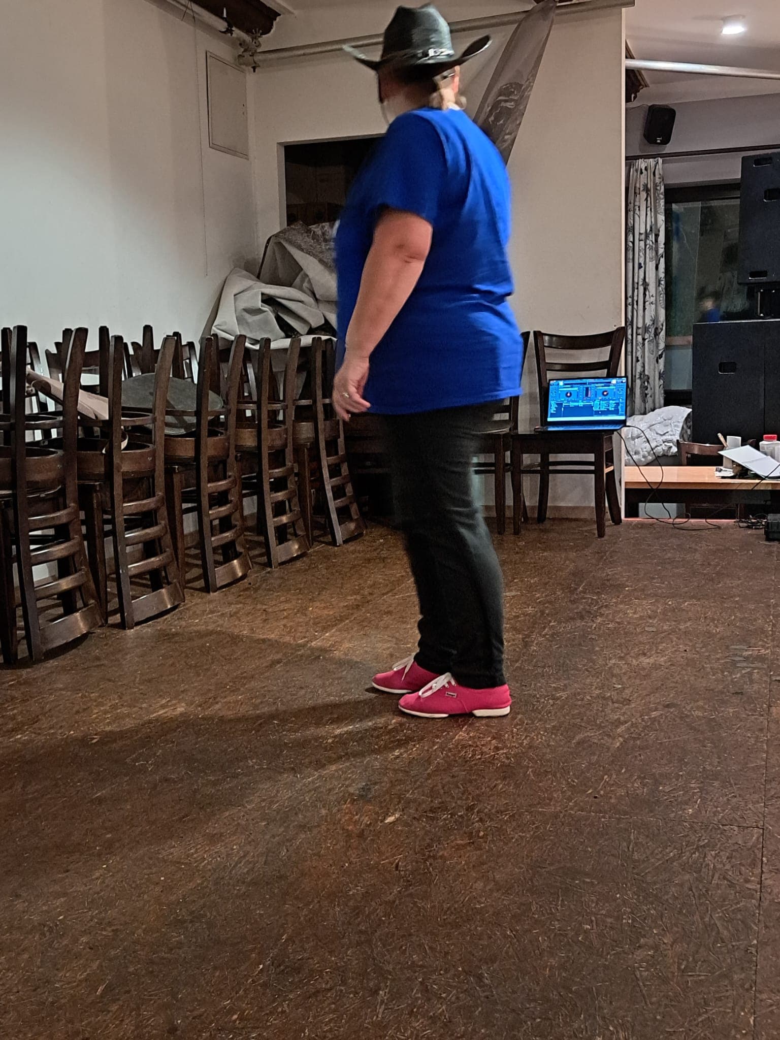 Die Trainerin mit Cowboyhut und pinken Schuhen von hinten, vorne das DJ-Pult